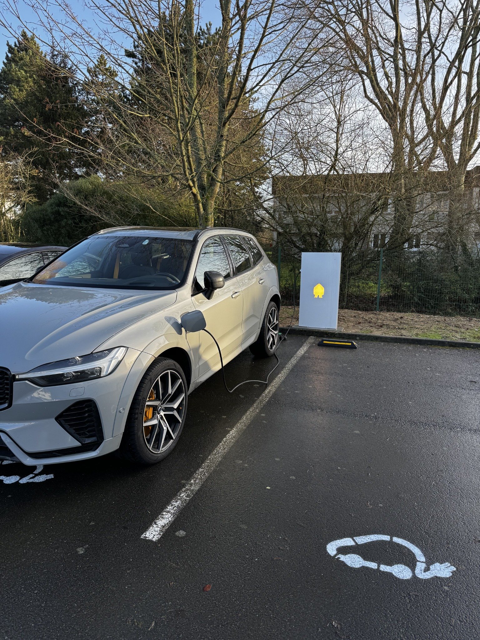 Véhicule raccordé à une borne de recharge sur un parking extérieur.