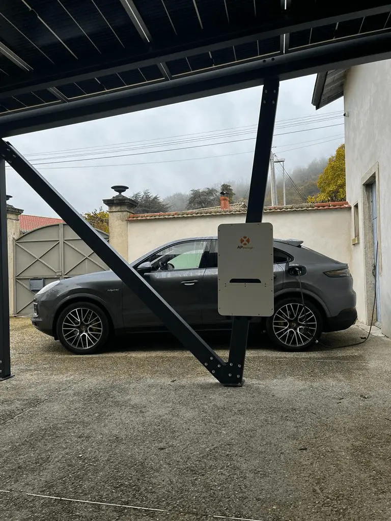 Véhicule sous un carport équipé de panneaux, près d’une borne de recharge.